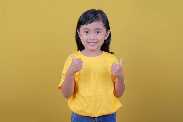 노란색 티셔츠를 입고 두 엄지 손가락을 사용하여 어린 아이의 미소