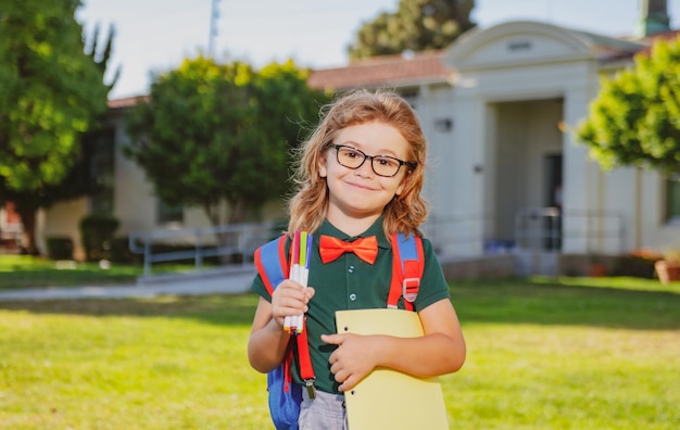 Smiling little school student wit backpack book portrait of happy young boy outside the primary scho