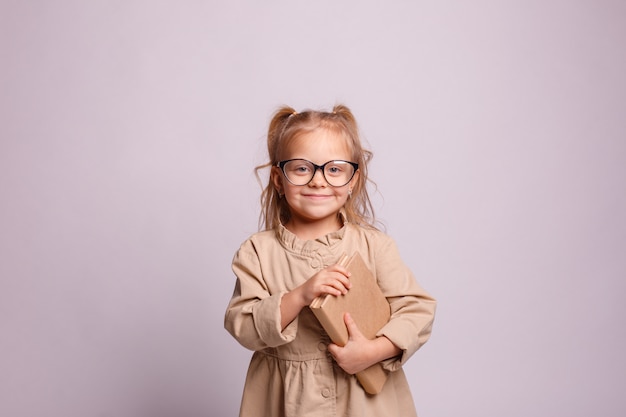 Smiling little schoolgirl girl in glasses with a book on a gray background. Place for text, banner