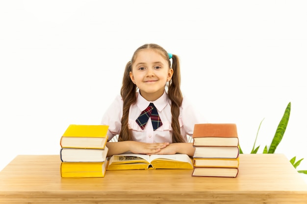 Smiling little student girl with many books at school