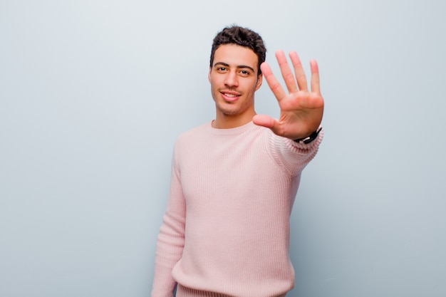 smiling and looking friendly, showing number five or fifth with hand forward, counting down