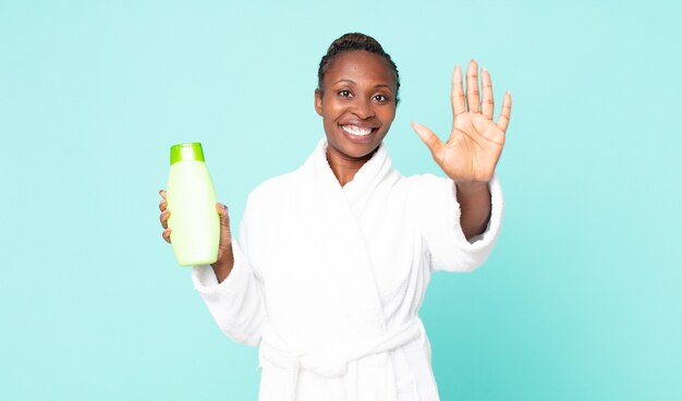 Smiling and looking friendly, showing number five wearing bath robe and holding a shampoo