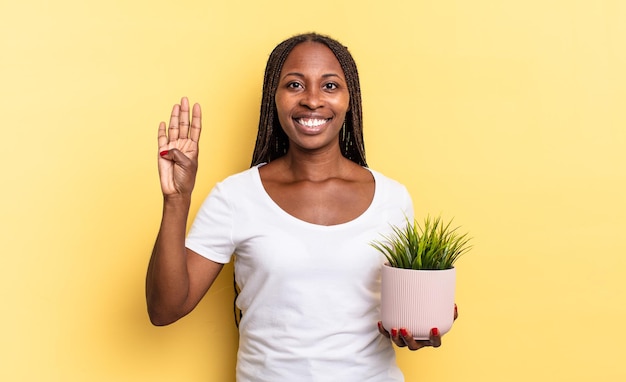 Smiling and looking friendly, showing number four or fourth with hand forward, counting down holding a plant pot