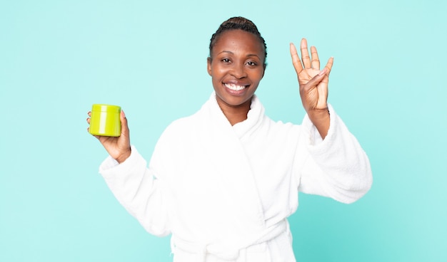 Smiling and looking friendly, showing number four wearing bath robe and holding hair mask