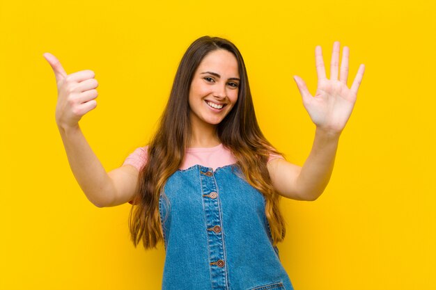 smiling and looking friendly, showing number six or sixth with hand forward, counting down