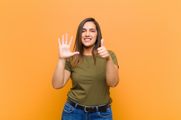 Smiling and looking friendly, showing number six or sixth with hand forward, counting down