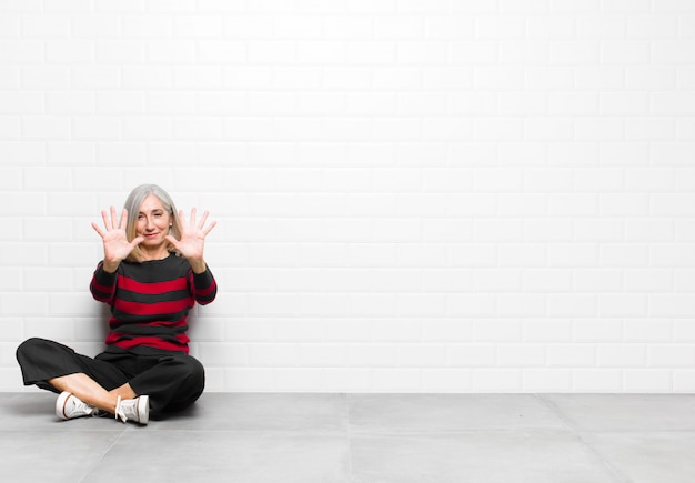 smiling and looking friendly, showing number ten or tenth with hand forward, counting down