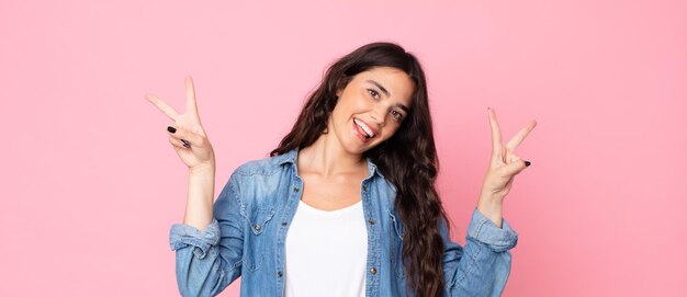 Smiling and looking happy friendly and satisfied gesturing victory or peace with both hands