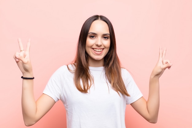 smiling and looking happy, friendly and satisfied, gesturing victory or peace with both hands