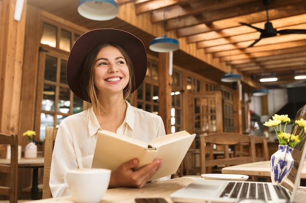 Sorridente bella donna con cappello seduto al tavolo del bar al chiuso