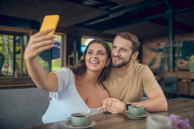 午後にカフェに座ってスマートフォンでselfieを取っている恋人の女性と男性の笑顔