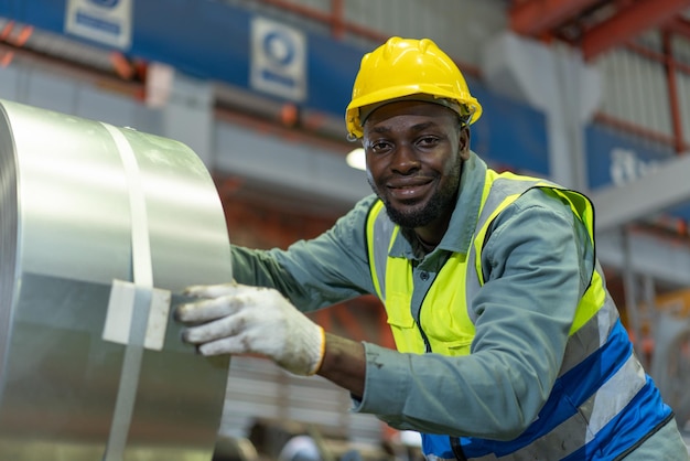 Smiling male black worker wearing safety vest with yellow helmet working at industry factory