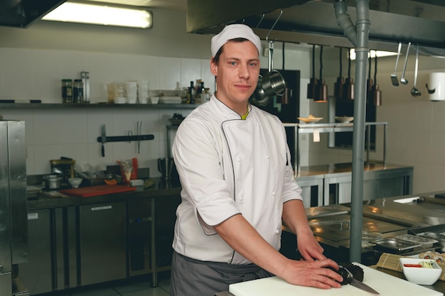 Foto chef maschio sorridente in uniforme che prepara sushi in una cucina del ristorante asiatico