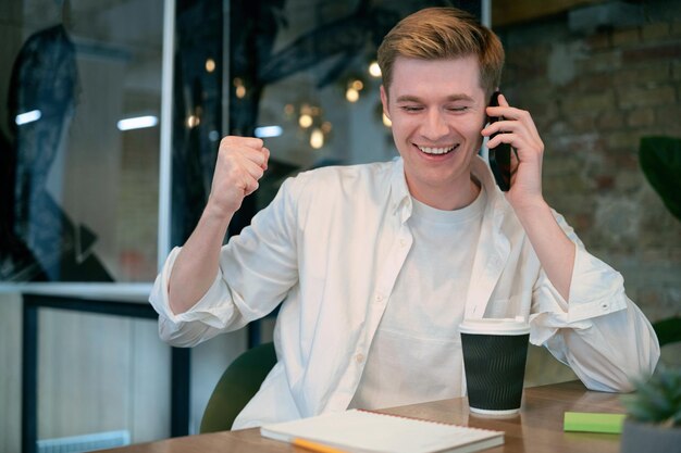 Smiling male coworker talks on smartphone sitting at table in office Business management concept