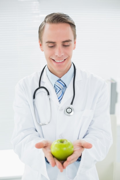 Smiling male doctor holding a green apple