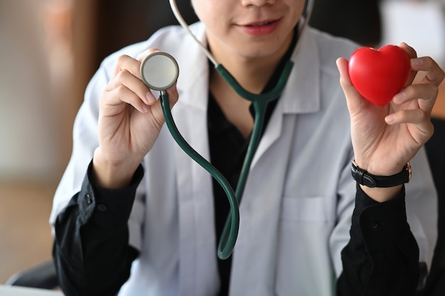 Smiling male doctor holding red heart and stethoscope. Health insurance concept.