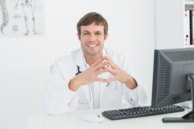 Улыбающийся мужчина-врач с компьютером в медицинском кабинете