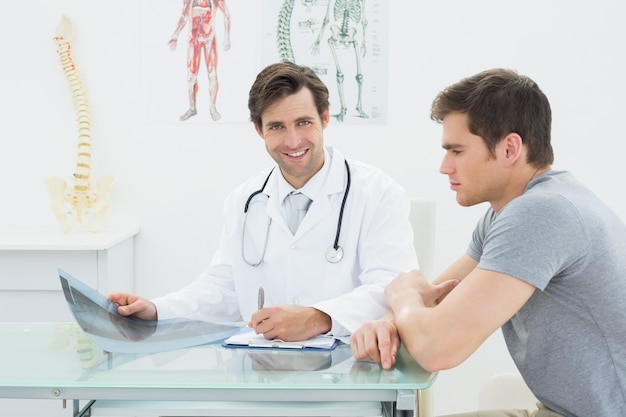 Smiling male doctor writing reports besides patient