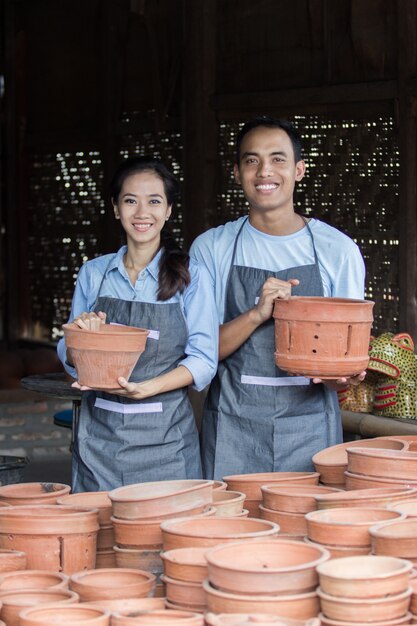 Photo smiling male and female potter holding their product in pottery