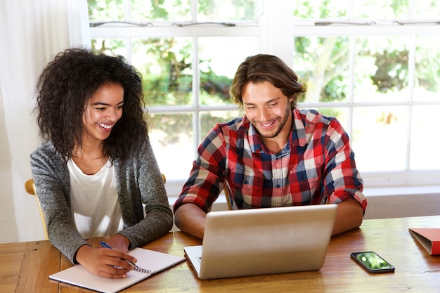 Smiling male and female students sitting at table with laptop