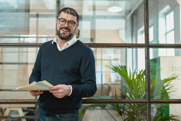 Foto responsabile maschio sorridente che tiene gli archivi di documento nell'ufficio