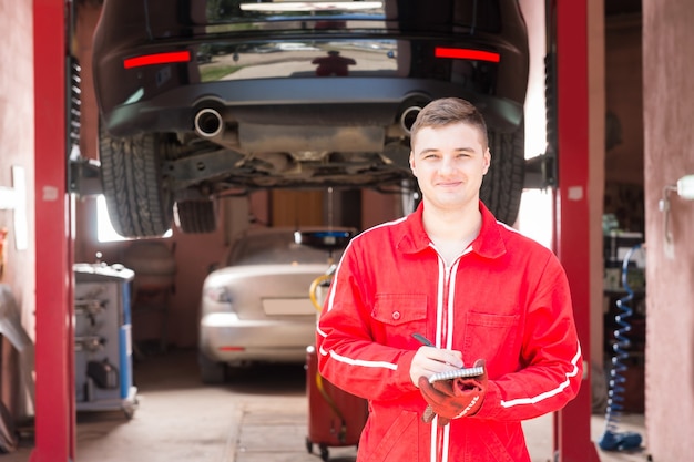 Smiling male motor mechanic standing making notes in front of a black sedan