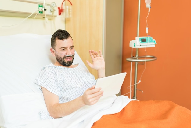 Paziente maschio sorridente che saluta durante la videoconferenza su tablet digitale in ospedale