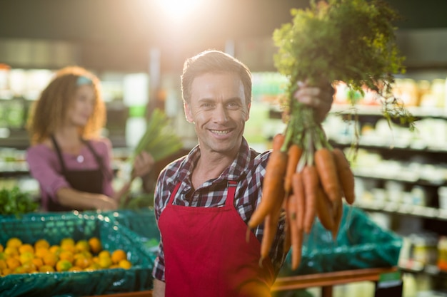 Smiling male staff holding bunch of carrots in organic section