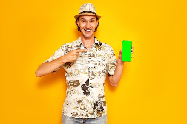 Photo smiling male tourist traveler points with index finger at green blank phone screen space for text