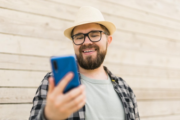 Il turista maschio sorridente usa lo smartphone durante la pausa estiva in città su tecnologie e soci di pareti in legno