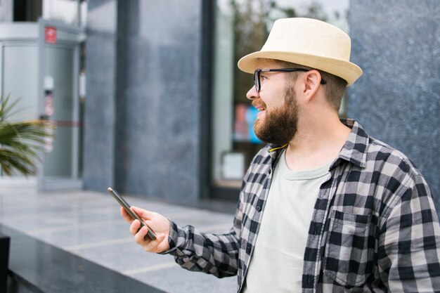 笑顔の男性観光客が夏の街の休憩技術とソーシャルメディアアプリのコンセプトの間にスマートフォンを使用