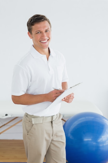 Photo smiling male trainer with clipboard in gym at hospital