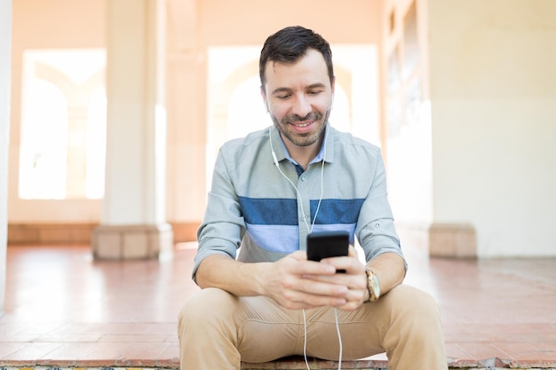 Улыбающийся мужчина использует радио для прослушивания музыки на смартфоне, сидя в коридоре