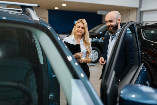 写真 車のディーラーで笑顔の男性と販売員。車両ショールームの顧客と販売者、輸送機関を購入する男性、自動車ディーラー事業