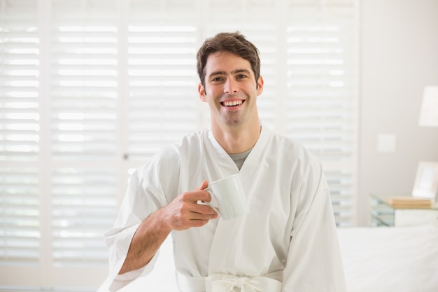 Smiling man in bathrobe drinking coffee in bedroom