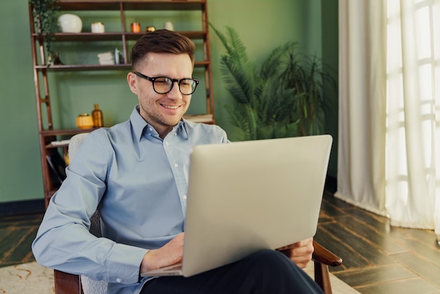 Smiling man in a blue shirt working on a laptop comfortable in a welldecorated indoor space