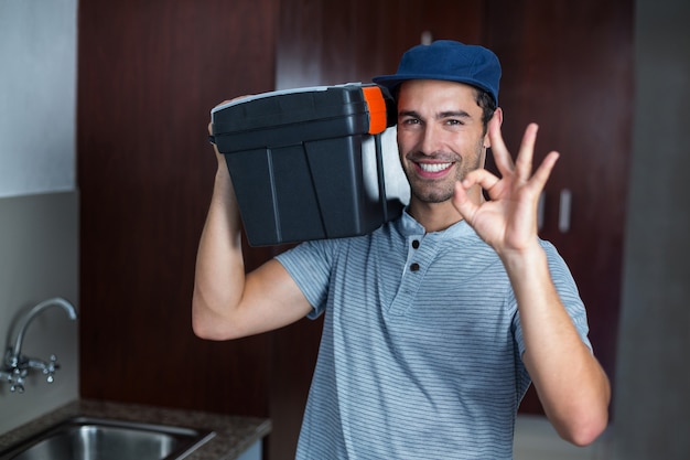 Smiling man carrying toolbox while showing ok sign 