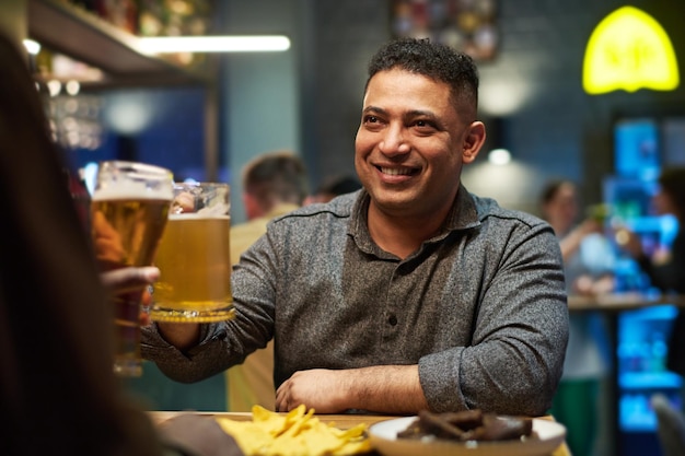 Smiling man in casualwear looking at his buddy during toast with beer