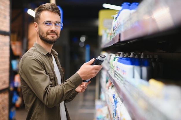 Smiling man chooses shampoo in supermarket