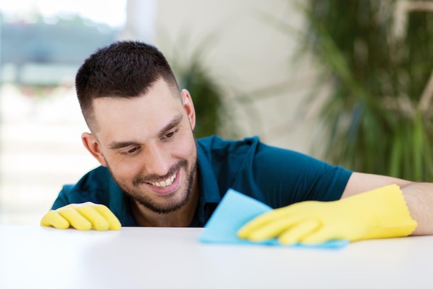 smiling man cleaning table with cloth at home