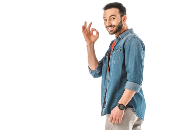 Smiling man in denim shirt showing okay gesture and looking at camera isolated on white