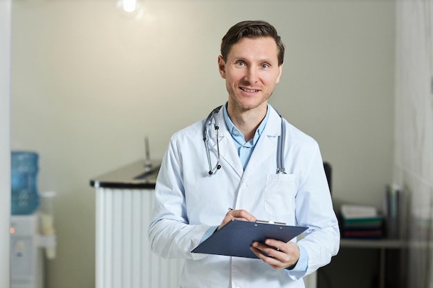 Smiling man doctor wearing lab coat in clinic and looking at camera