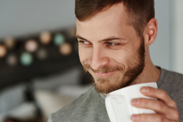 寝室でコーヒーを飲む笑顔の男