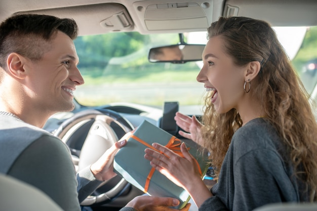 Smiling man giving box to joyful woman in car