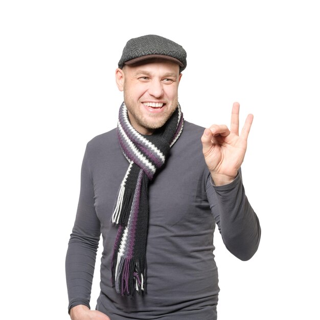 Улыбающийся мужчина в серой шляпе и сером шарфе показывает знак "хорошо"