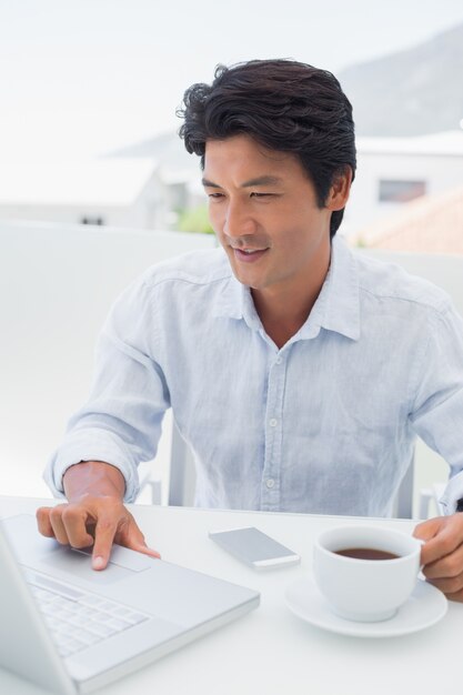 Smiling man having coffee and using laptop