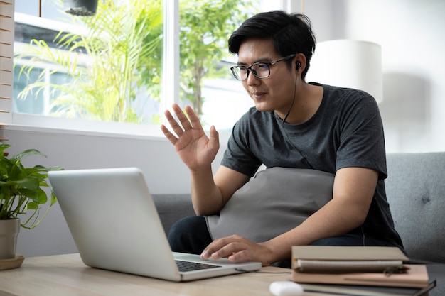 Smiling man having video call with computer laptop on sofa in living room.