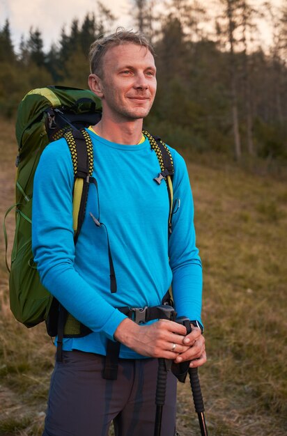 山の草が茂った丘の上に立っている笑顔の男のハイカー