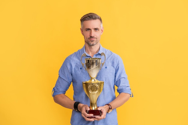 Smiling man hold champion cup on yellow background victory