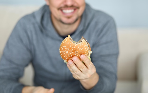 Smiling man hold fresh burger in hand background Fast food delivery concept